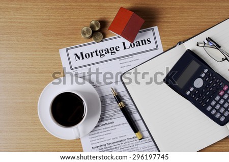 Mortgage loans concept with worktable and coffee cup and fountain pen and calculator and eyeglasses and house paper and coins stack