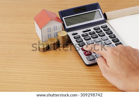 Hand on calculator with coins stack and paper house for mortgage loans concept