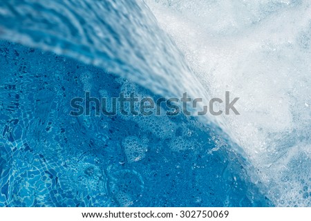A small waterfall in the pool. Water from an artificial waterfall pours into the pool and up white foam bubbles.