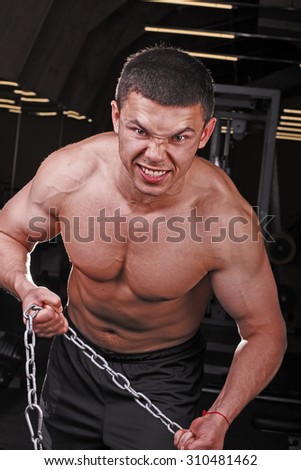 Young strong muscular man trying to break the chain. A young bodybuilder in the gym. A young man with a gorgeous body in training.