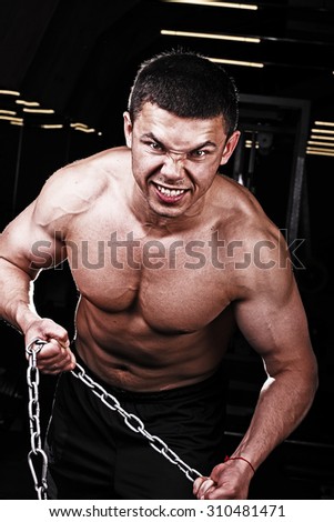 Young strong muscular man trying to break the chain. A young bodybuilder in the gym. A young man with a gorgeous body in training. Processing in the style of the magazine Eksvayr.