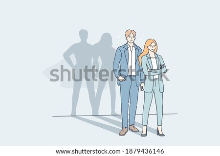 Successful cooperation and business team concept. Young man and woman business people partners standing together with big hero superman shadows on wall meaning strength of unity 