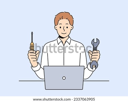 Man repairs laptop after breakdown and holds screwdriver and wrench in hands, working as system administrator. Guy fixes laptop or wants to upgrade by replacing hard drive of computer