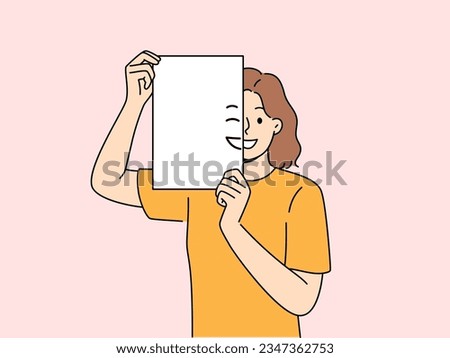 Smiling woman holding piece of paper with emoji in front of face and looking at screen. Positive girl with partially painted smile is sharing good mood and positive emotions with you.