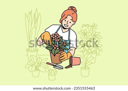 Woman florist takes care of home plants and holds flower pot with blooming violet standing near table. Girl in apron enjoys job as florist, and makes career as salesperson in store or greenhouse