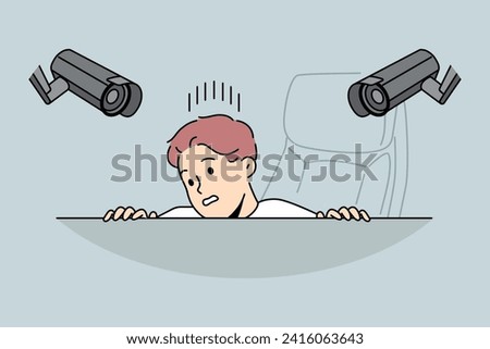 Surveillance cameras above workplace make man feel discomfort and hide from constant monitoring. CCTV system of two cameras in office above workspace, for understanding of big brother