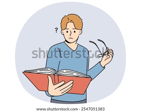 Man with book takes off glasses, trying to make out text in textbook and getting upset because of deterioration of vision. Guy is experiencing vision problems associated with excessive eye strain.