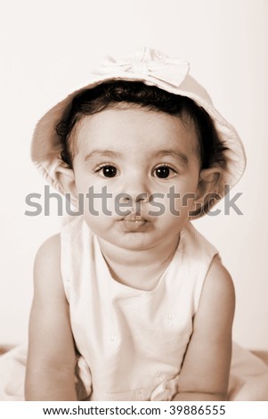 Beautiful baby looking at the camera wearing a hat, sepia image