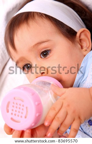 baby girl with dress and hair band and pink bottle over bed