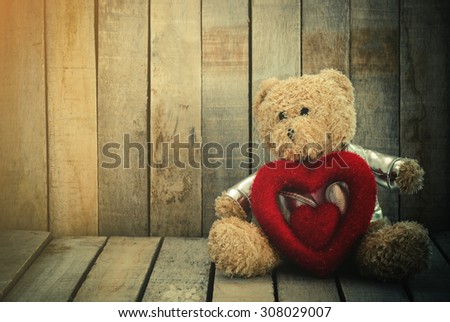 Teddy bear hugging a heart shape on wood.