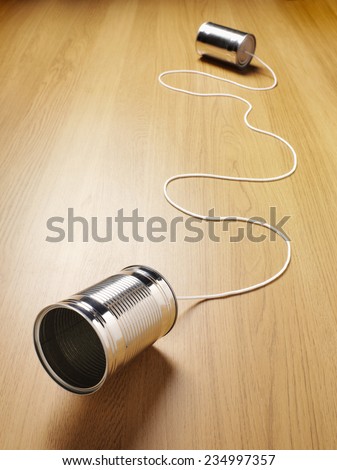 Two tin cans joined with a cord on a wooden background for primitive communication and copy space