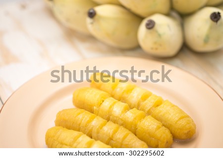 Fresh and delicious boil yellow banana with coconut milk on brown metal plate on wood  for local Thai dessert background