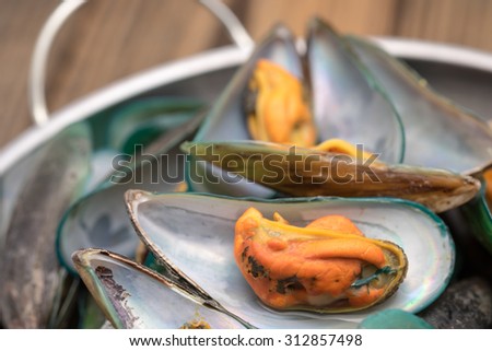 Fresh and steamed green mussels with herb in silver pot on wood table for seafood cuisine background