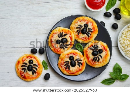 Halloween mini spider pizzas made from.pizza crust,pizza sauce,olive oil,mozzarella cheeses and black olives on plate with white wood table background.Art food idea per kids halloween party.Copy space