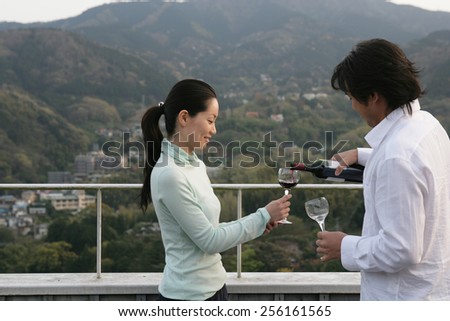 Side profile of a young man pouring red wine into a young woman s glass