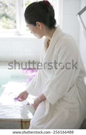 Side profile of a young woman sitting at the edge of a bathtub