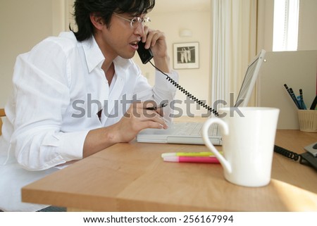 Young man using a laptop and talking on the telephone
