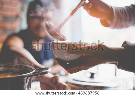 A person uses a ladle to pour soup into a bowl in a soup kitchen