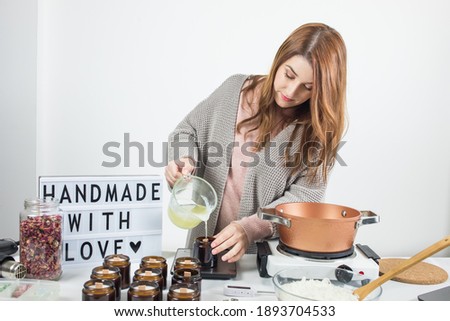 Woman pouring melted wax into amber candles container. Ecological and vegan business. Soya wax candle accessories. Handmade with love. Remote work, online shop, workplace