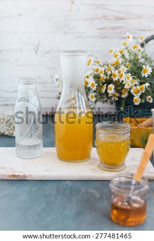 Bio organic and fresh summer beverage for bottle, jar of honey with chamomile bouquet over on rustic blue table.