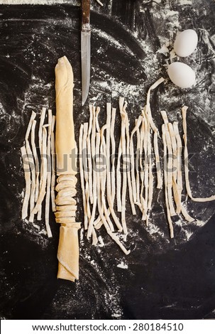 Still life with homemade fresh pasta with knife from above dark board. Composition food concept.