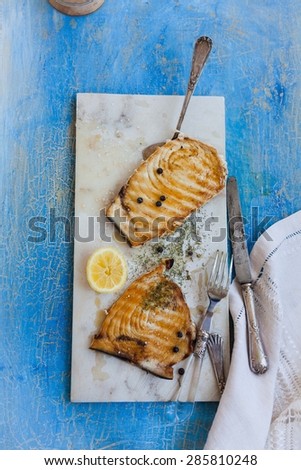 Grilled tuna steak served on marble table over on blue rustic table with kitchen tools and linen napkin. Rustic style.