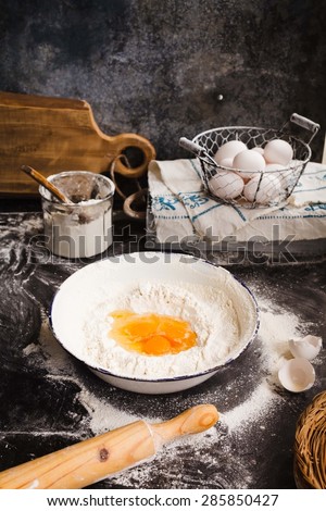 Baking cake ingredients. Bowl, flour, eggs, egg whites foam, eggbeater, rolling pin and eggshells on black chalkboard. Cooking course poster. Rustic dark style.
