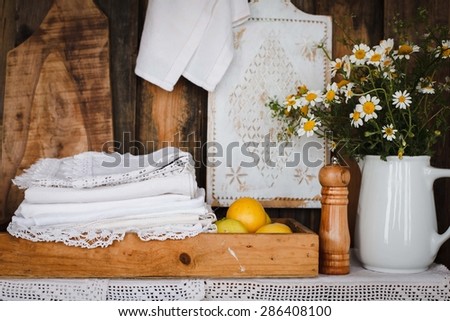 Still life with vintage linen embroidery white napkin over on shelves with pottery with simmer flowers and decorative white cutting board. Rustic style