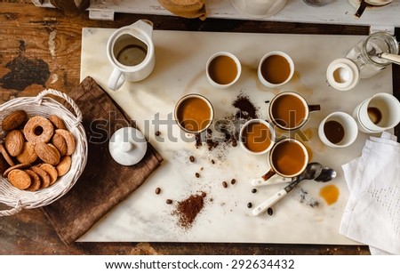 A coffee drink family breakfast concept. Concept include many cups with cappuccino and coffee drink situated over a marble rustic kitchen table with basket of biscuits from above. Rustic still life.