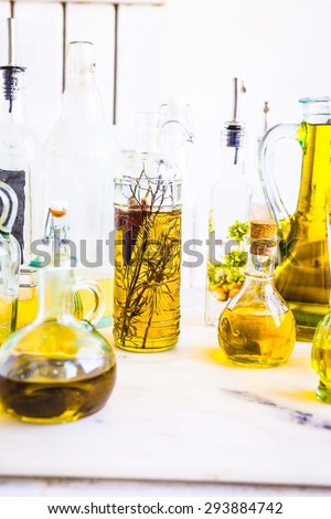 Glass bottles of refined and olive oil with spices and herbs over on the marble table on white wooden background. Rustic style.
