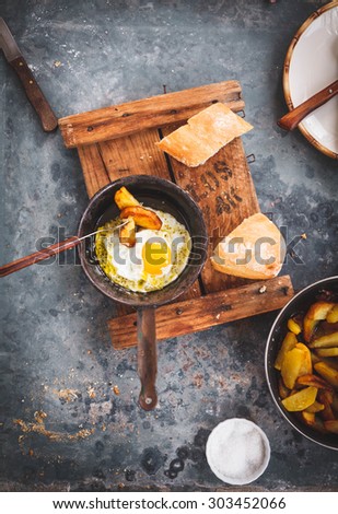Simple homemade dish of fried egg in a frying old pan served on a rustic chalkboard from above on blue rustic table with pan of fried potatoes. Rustic composition of traditional homemade meal concept.