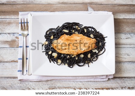 Roasted chicken with black spaghetti, maple syrup and almonds in white plate and on a wooden desk, top view