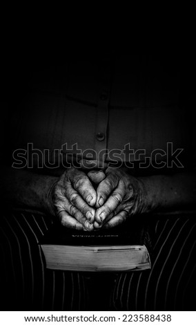 Elderly woman holds bible and prays black and white