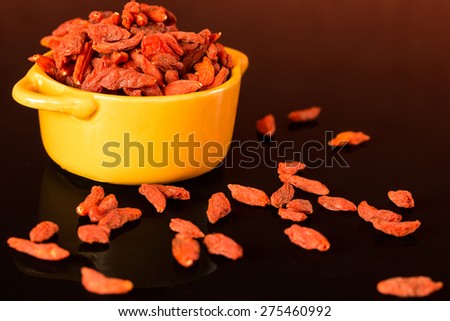 Dried goji berries in orange bowl isolated on black background. Culinary healthy snack.