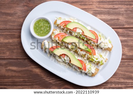 
Mexican flutes, golden tacos. Traditional Mexican food. Traditional Mexican tacos with tomato, avocado and green hot sauce. Gourmet mexican food