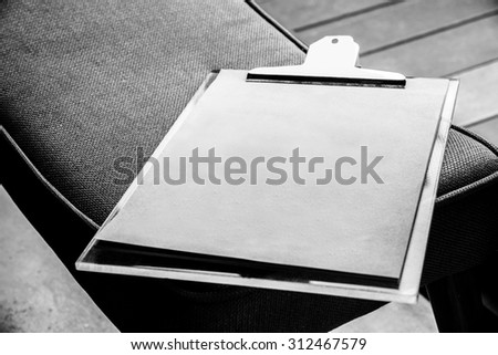 black and white color photo of  paper menu in clip plate put on cloth bench  with  list and empty space for text