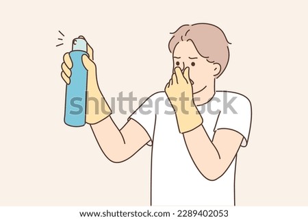 Dissatisfied man with aromatic spray to remove unpleasant odors covers nose with hand while spraying freshener. Householder guy uses air freshener to mask smell in unventilated room 