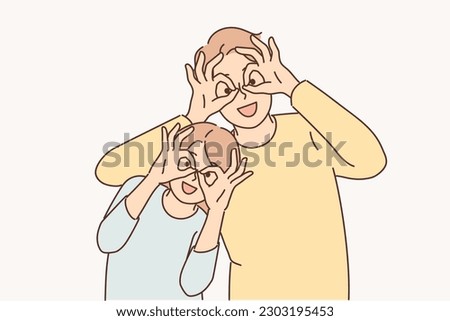 Happy father and daughter make funny faces to have fun putting fingers to eyes instead of glasses. Happy family of man and teenage girl having rest together posing with funny grimace