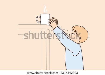 Boy reaches for mug of hot tea on table at risk of getting burned and getting into trouble because of negligence of parents. Small child wants hot drink and needs adult help to avoid health risks.