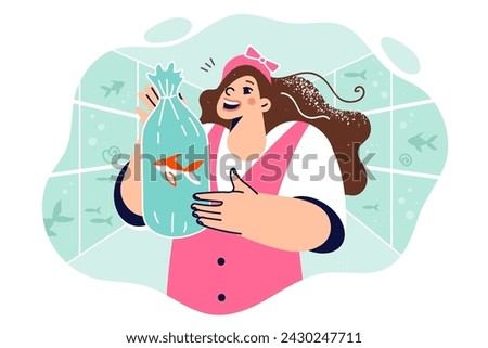 Little girl holds live fish inside polythene bag with water, standing in oceanarium with large aquariums. Happy schoolgirl bought aquarium fish rejoices at appearance of new pet and friend