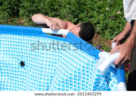 Assembling a swimming pool for bathing children in the country. A man builds a swimming pool for the kids outdoors. Blue portable swimming pool is almost ready before using.  ストックフォト © 
