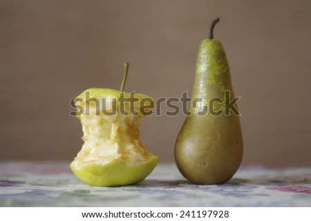 The eaten-around yellow apple and green pear on a table on a brown background/ The eaten-around apple and green pear