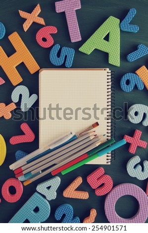 Notebook, pencils, felt-tip pens, brush against color letters and numbers / School supplies on a green table in an environment of color letters of the alphabet and numbers. Back to school background