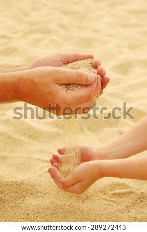 Father and the son pour sea sand from hand to hand on a beach.Hands of the man and the child with sand
