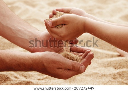 Father and the son pour sea sand from hand to hand on a beach.Hands of the man and the child with sand