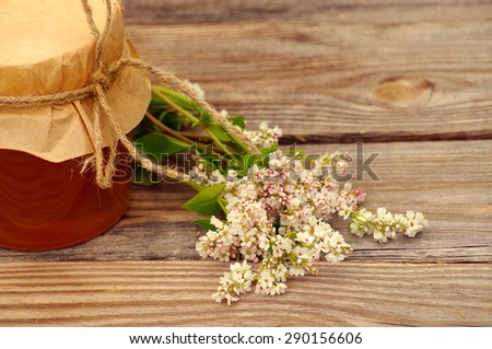 Honey in a glass jar with flowers of a buckwheat  on the wooden surface. Honey with flower