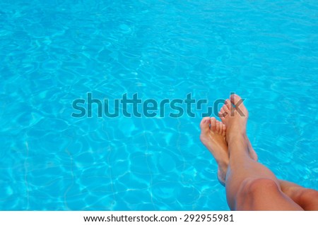 Woman\'s feet against blue water of the pool. Feet in the pool