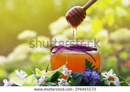 Honey in a glass jar the tied gift tape with a bow with June flowers melliferous herbson. Honey with flowers