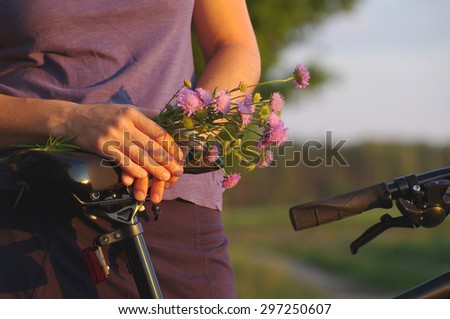 Girl's hands with a bouquet of wild flowers by bicycle. Girl with flowers and the bicycle