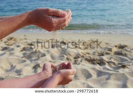 Mother and the son pour sea sand from hand to hand on a beach.Hands of the man and the child with sand